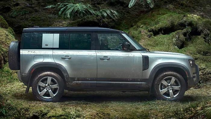 Profile of a silver Land Rover Defender in front of a forest.