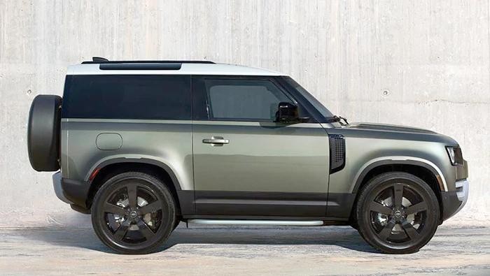 Profile of a green Land Rover Defender in front of a concrete wall.