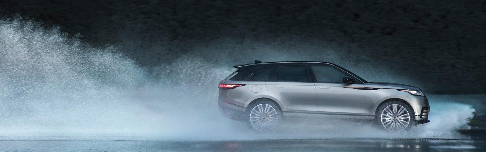 Profile view of a Range Rover Velar driving on a wet road.