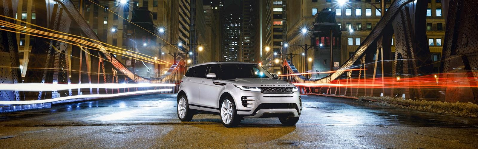 A silver Range Rover Evoque parked on a city bridge at night.