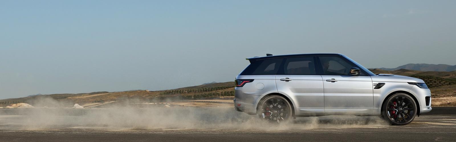 Profile view of a silver Range Rover Sport kicking up dust on a country road.