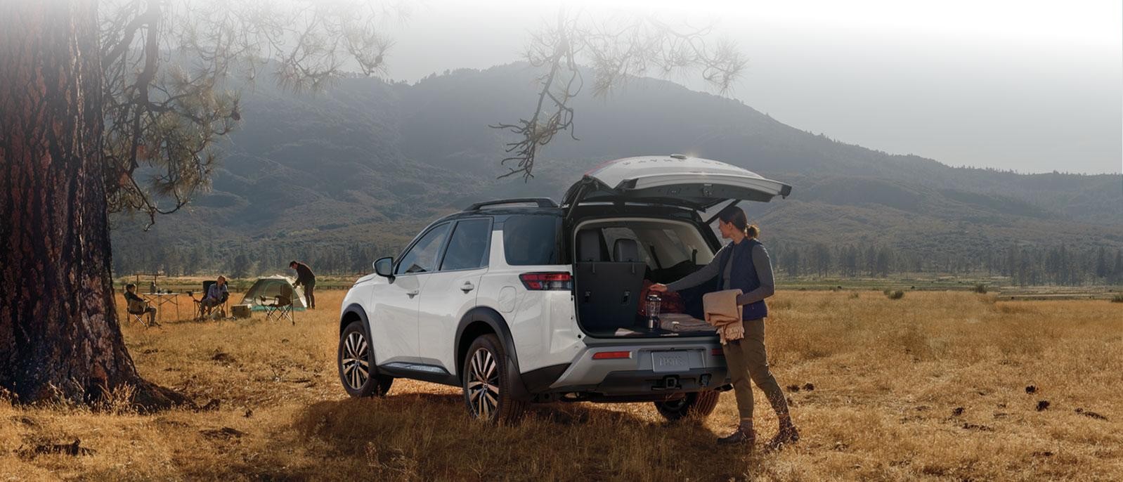 White 2025 Nissan Pathfinder in a field of grass with a family camping and mountains in the background