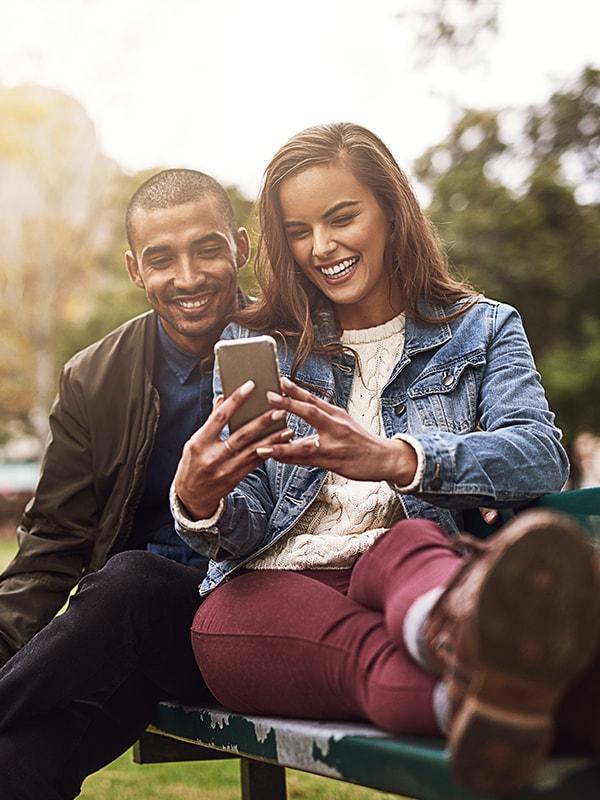 Smiling couple looking at a phone on a park bench