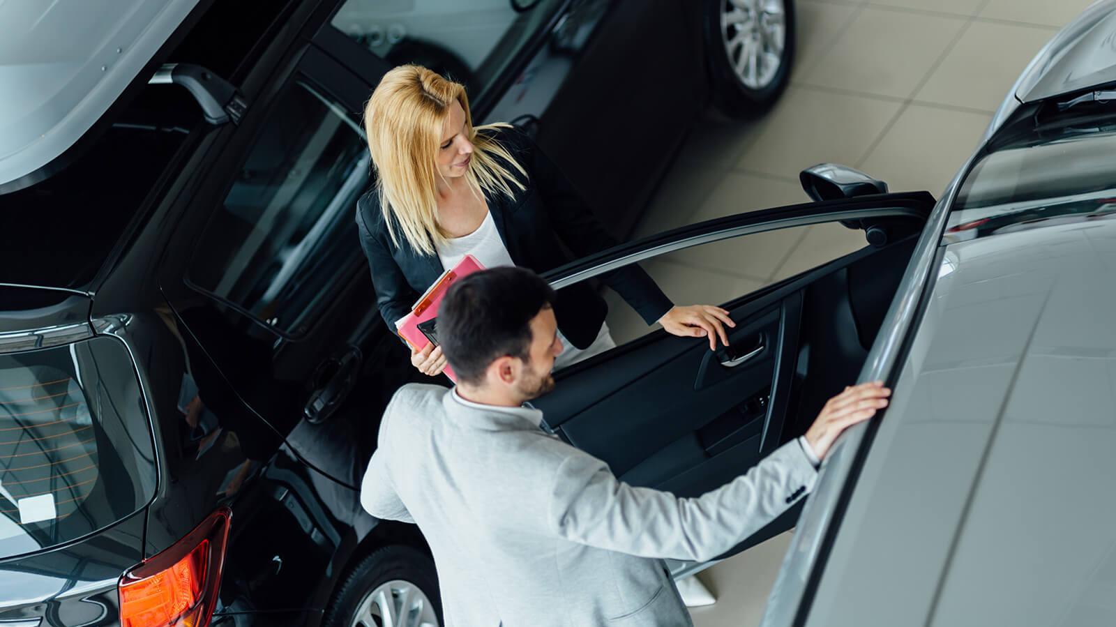 Dealership sales associate showing a customer a new car