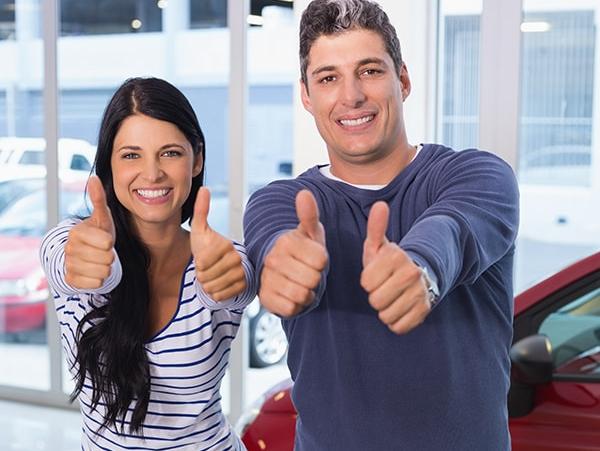 Smiling couple giving the thumbs up sign in a dealership