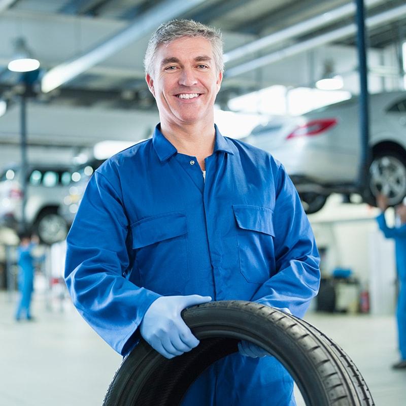 Smiling service mechanic in a garage holding a tire