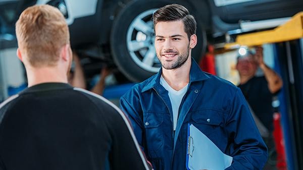 Mechanic holding a clipboard shaking a customer's hand