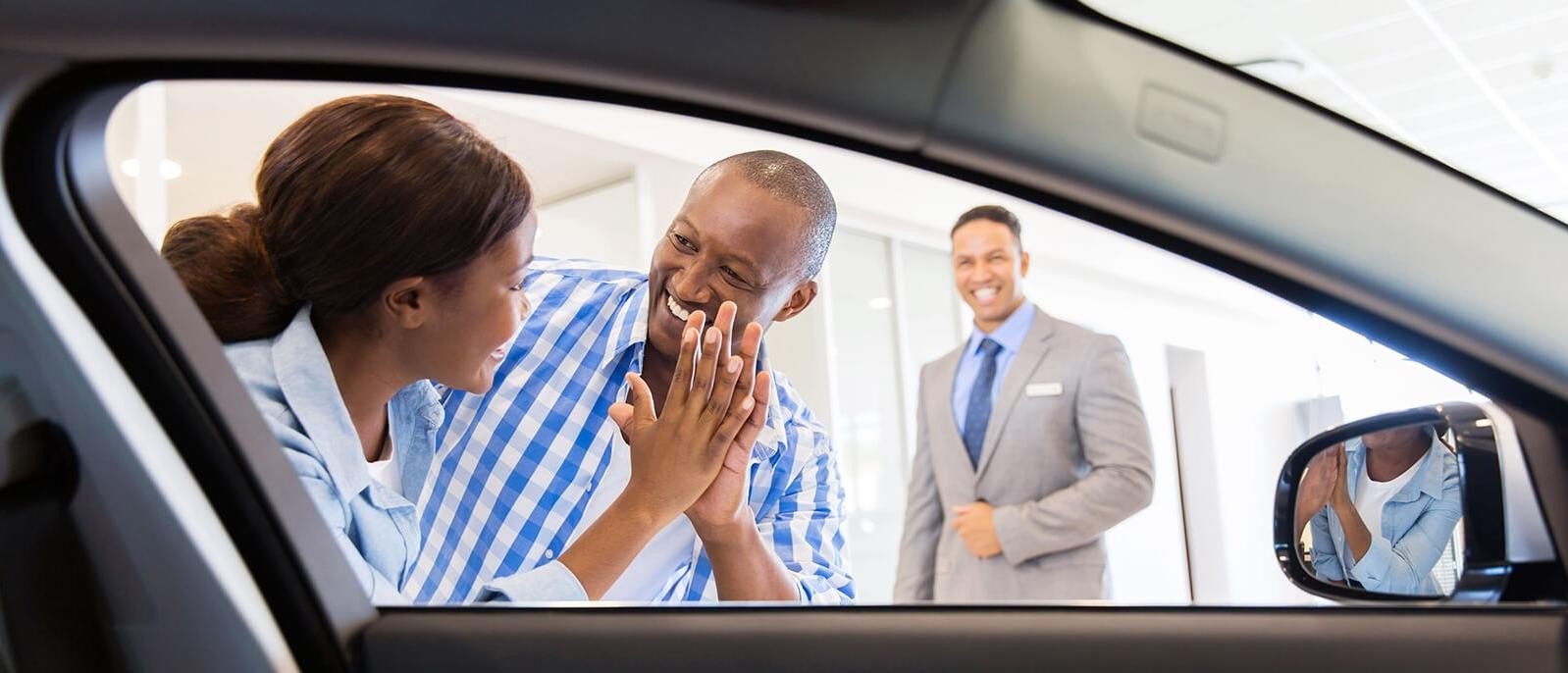 Smiling couple giving each other a high five in a car dealership showroom