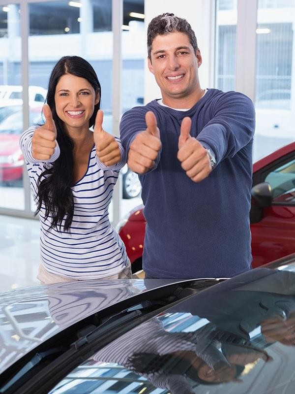 Smiling couple giving the thumbs up sign in a dealership