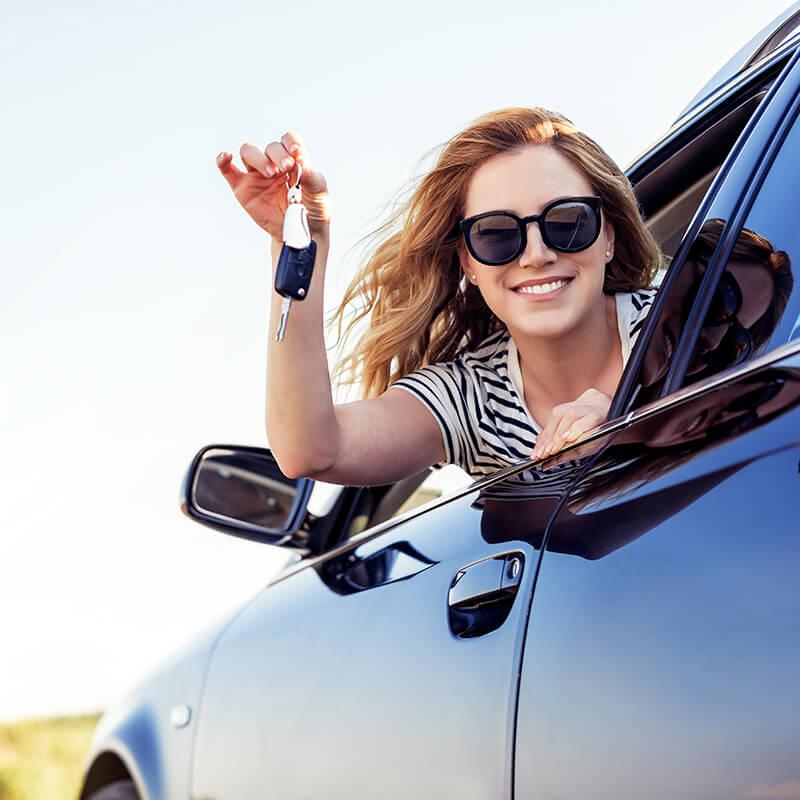 Smiling woman with sunglasses holding her keys in a car