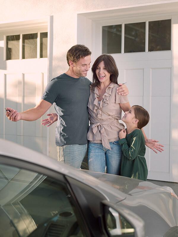 Smiling family looking at a new car parked in their driveway