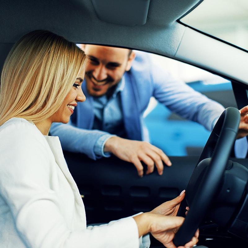 Woman sitting in a new car with a salesman in a dealership
