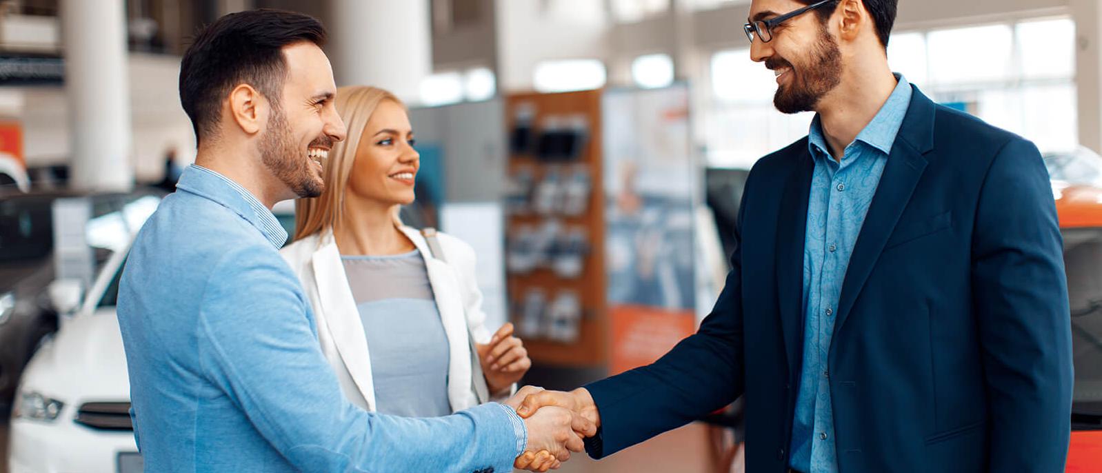 Couple shaking hands with a dealership sales associate