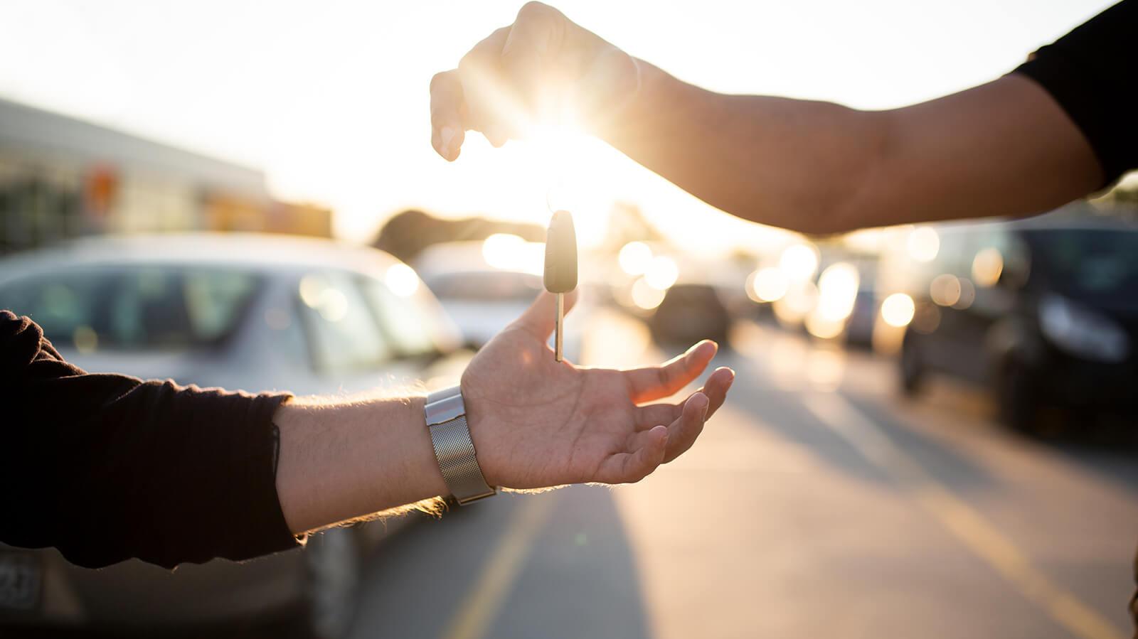A man's hand giving a car key to another man's hand