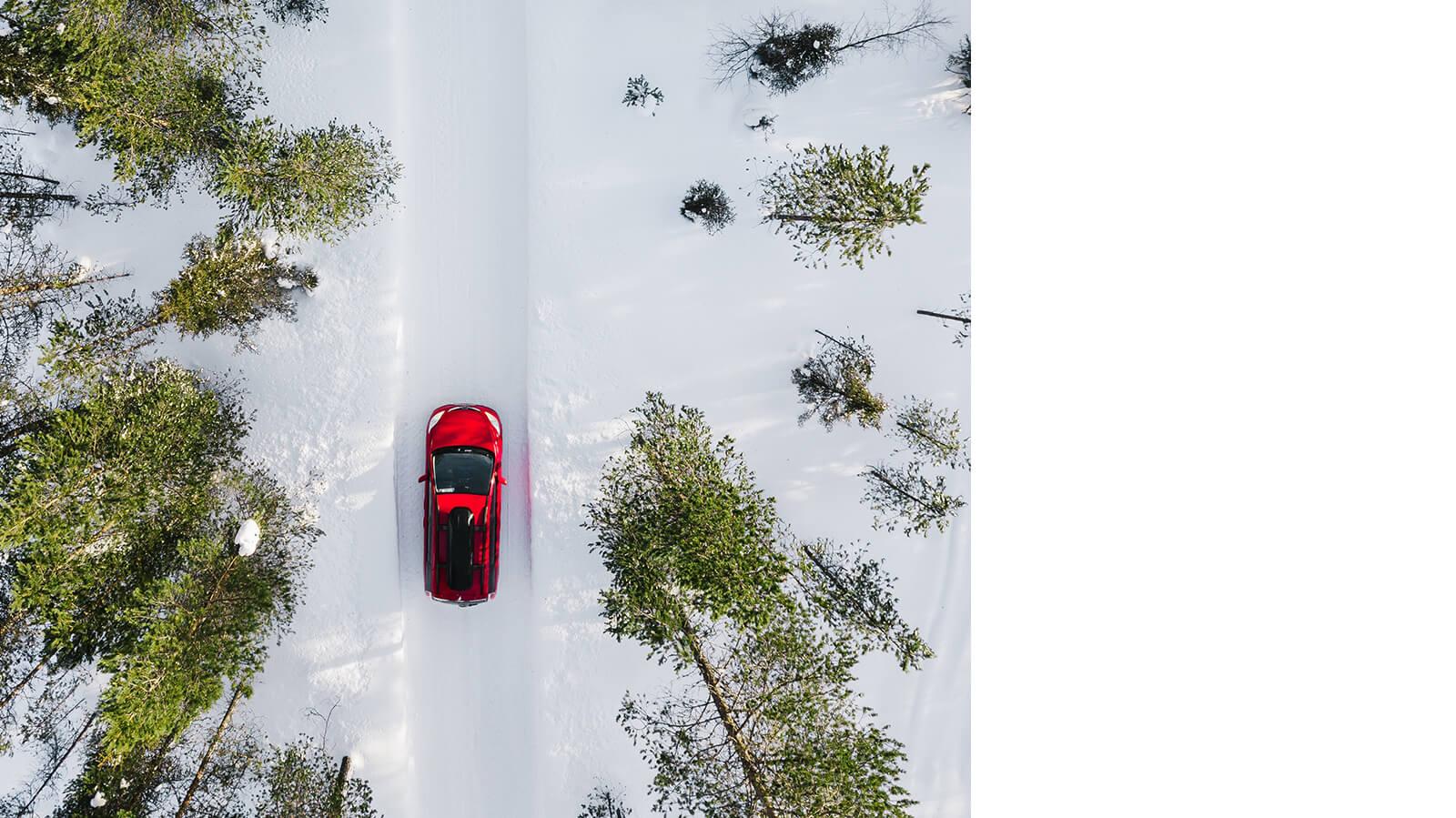 Aerial view of a red car driving in a snow covered forest