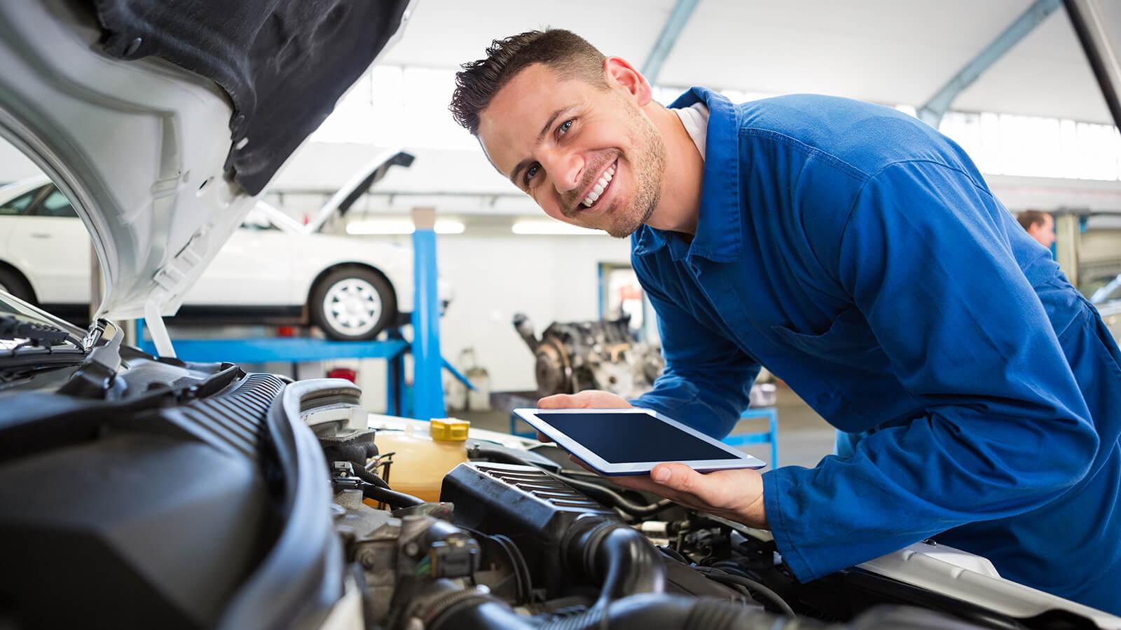 Smiling service mechanic inspecting a car's engine