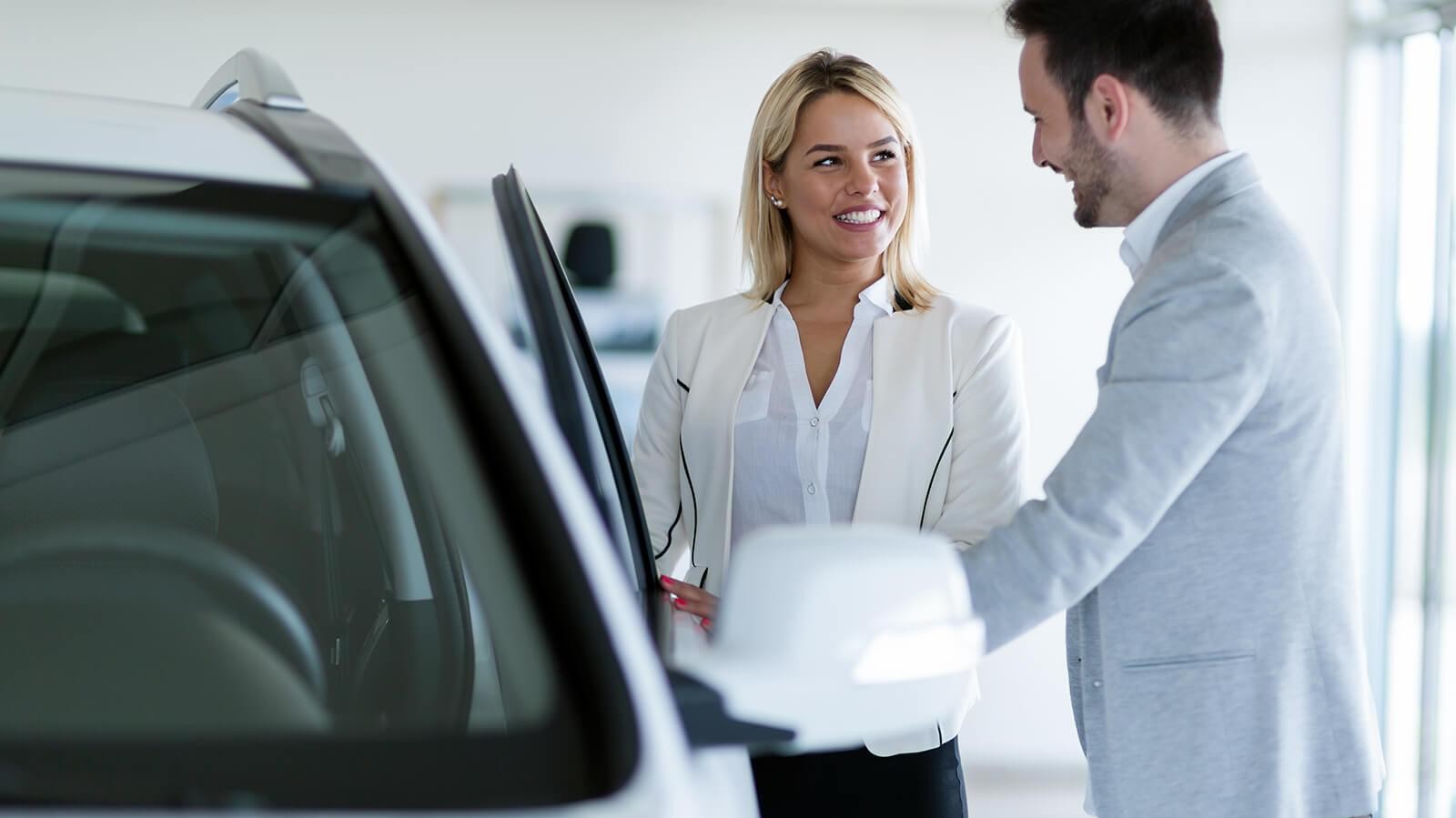 Dealership sales associate showing a customer a new car