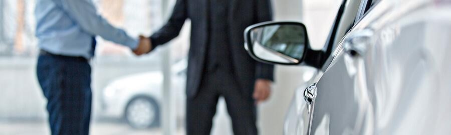 Two men in a car dealership shaking hands.