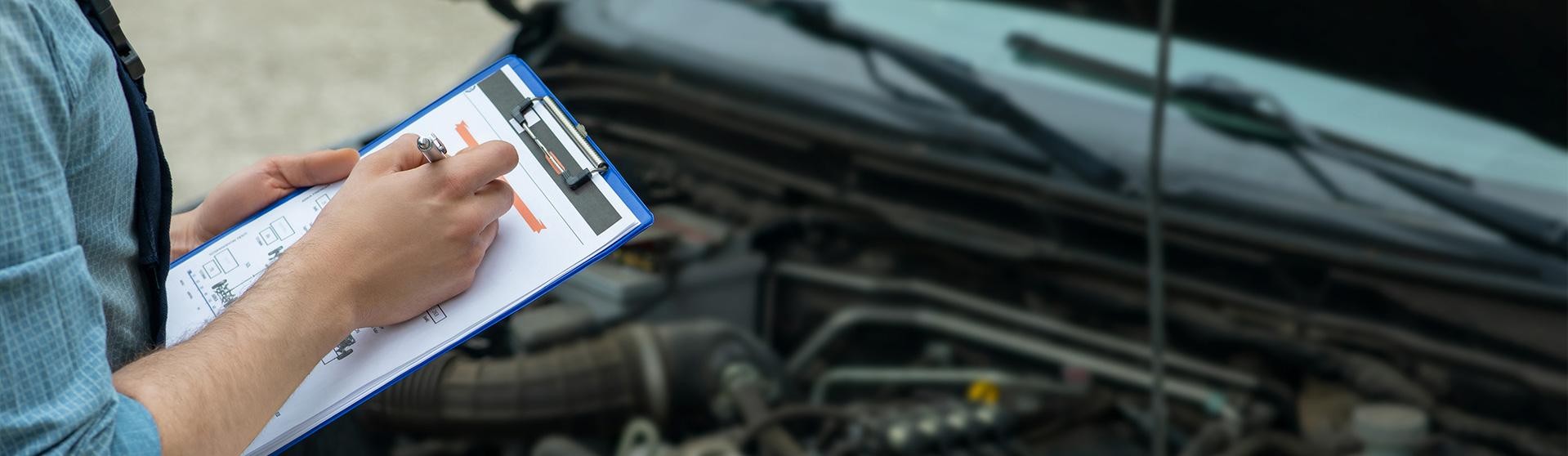 Man writing car checklist while working in auto repair shop.