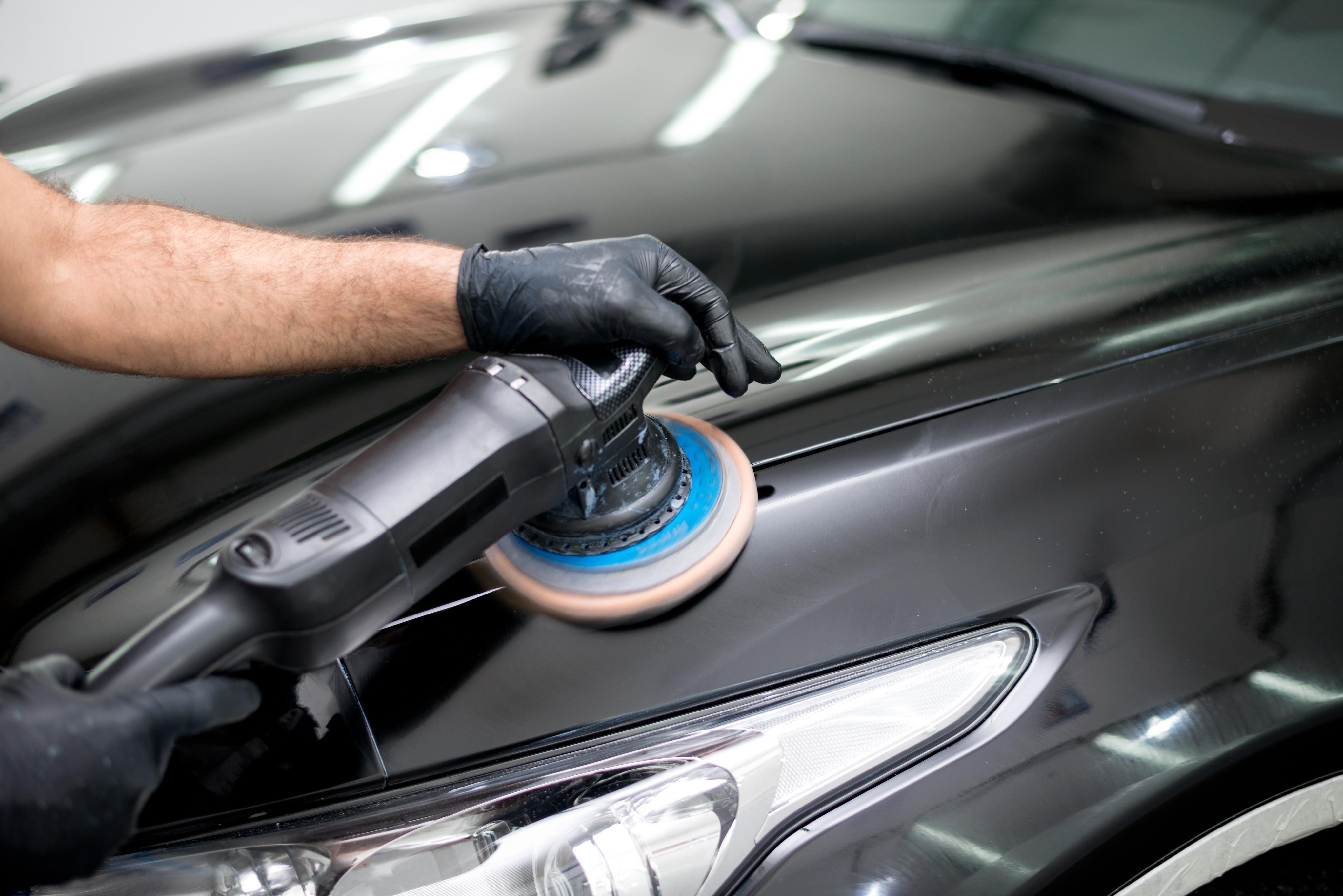 Man holding polishing tool on black vehicle body 