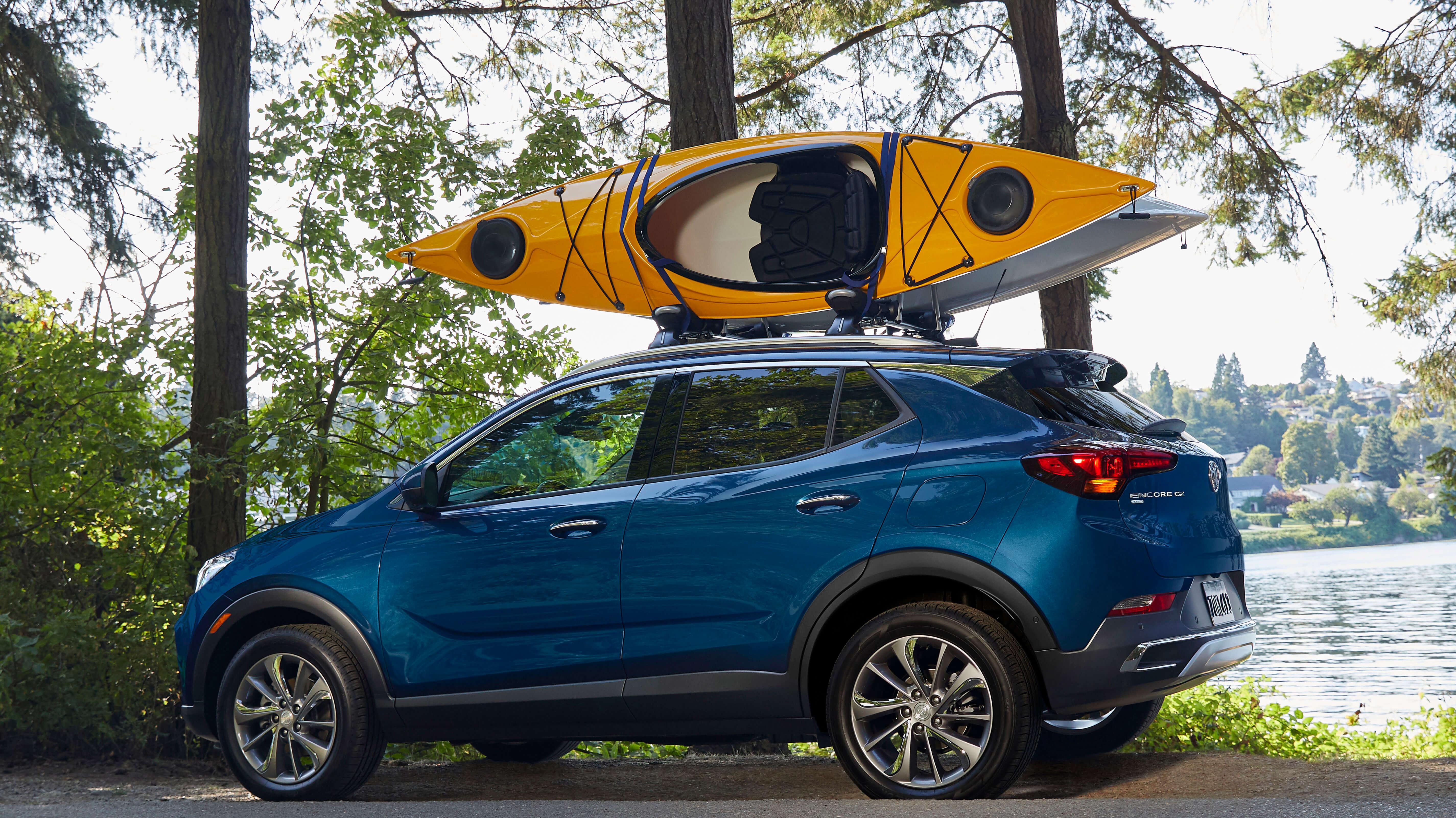 A Buick SUV with a kayak is parked near a lake.