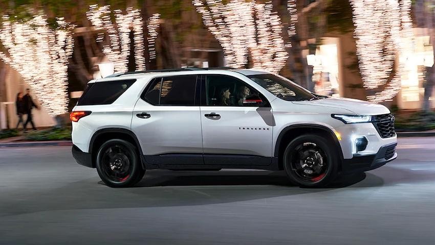 2023 Chevy Equinox driving in the street with two passengers in front of trees with lights