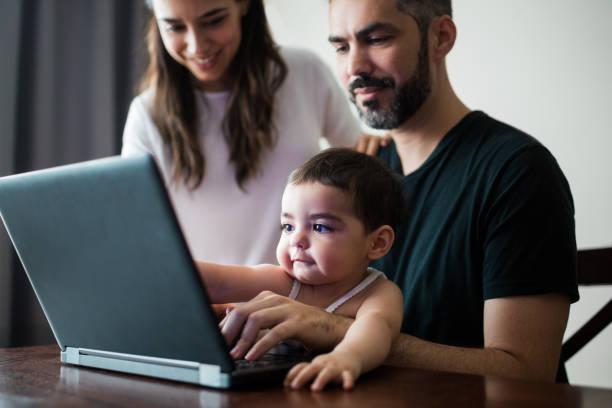 Latin parents and baby girl looking at laptop and smiling stock photo