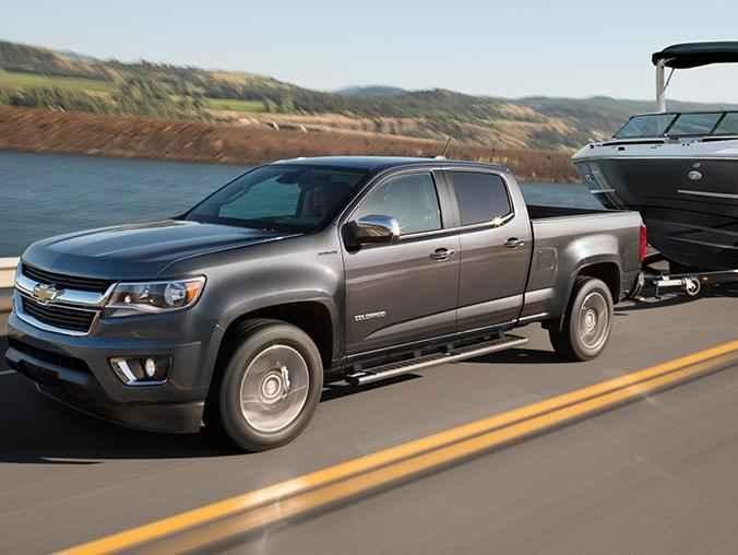 A Chevy Colorado towing a boat along a highway, next to a lake.