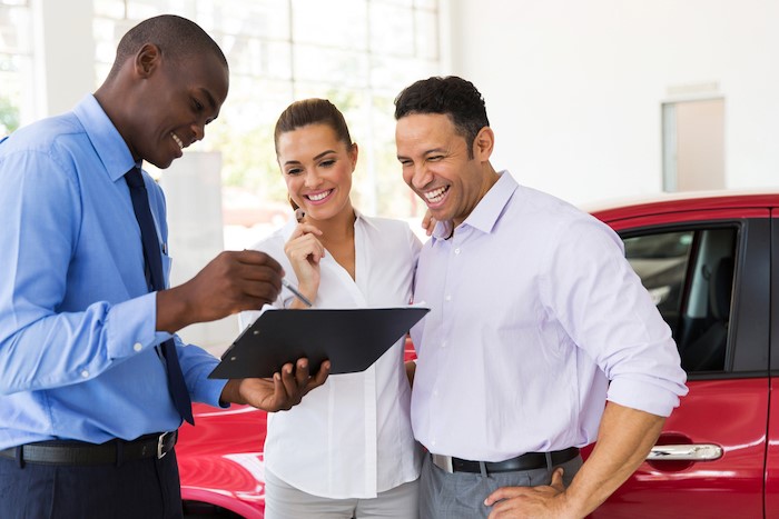 Young couple talking to car salesman about buying a used car