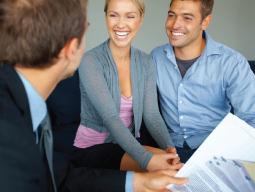 couple smiling, sitting across from salesperson holding a contract