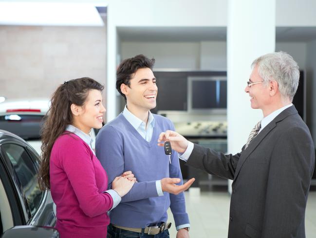 Happy couple with a dealership sales associate looking at a new vehicle