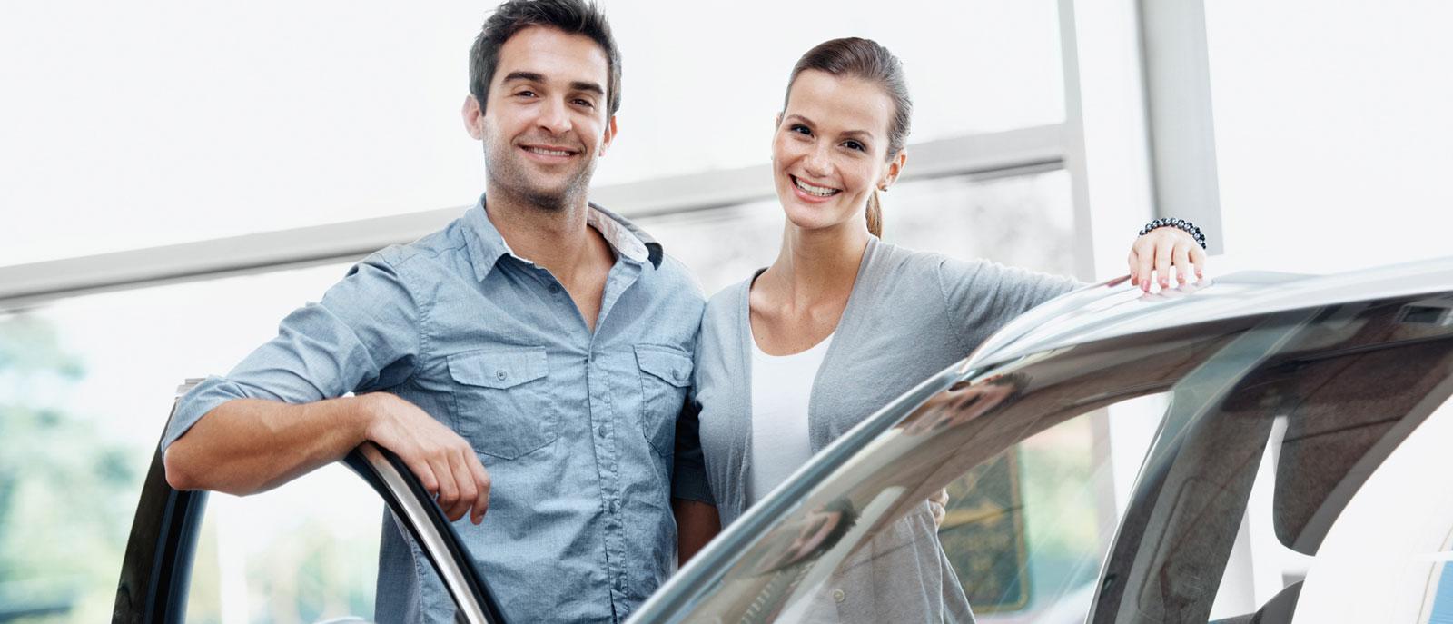Smiling couple  in a dealership standing besides a new vehicle