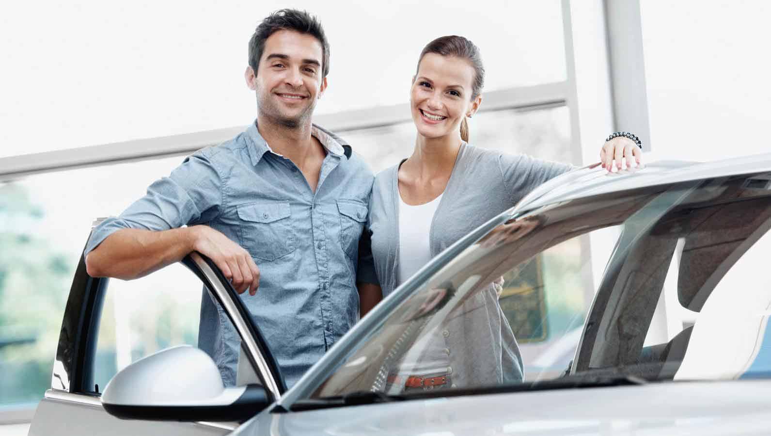 Smiling couple  in a dealership standing besides a new vehicle