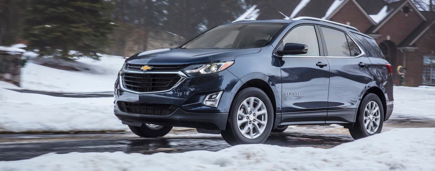 A dark blue 2019 Chevy Equinox is driving on a snowy suburban road after leaving a Staten Island used car dealer.