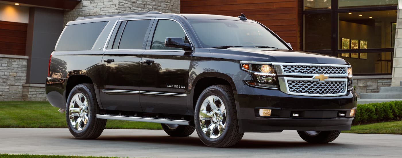A black 2018 Chevy Suburban is parked in front of a modern home after leaving an Elizabeth used car dealer.