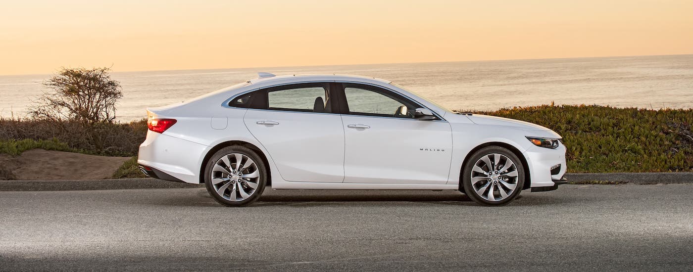 A white 2018 Chevy Malibu is shown from the side parked in front of an ocean after leaving a New Jersey used Chevy dealer.