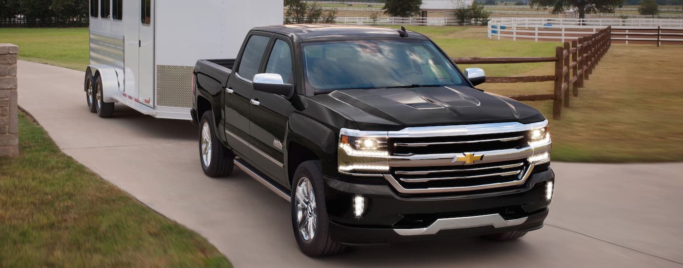 A black 2018 Used Chevy Silverado 1500 is towing a white horse trailer out of a farm.
