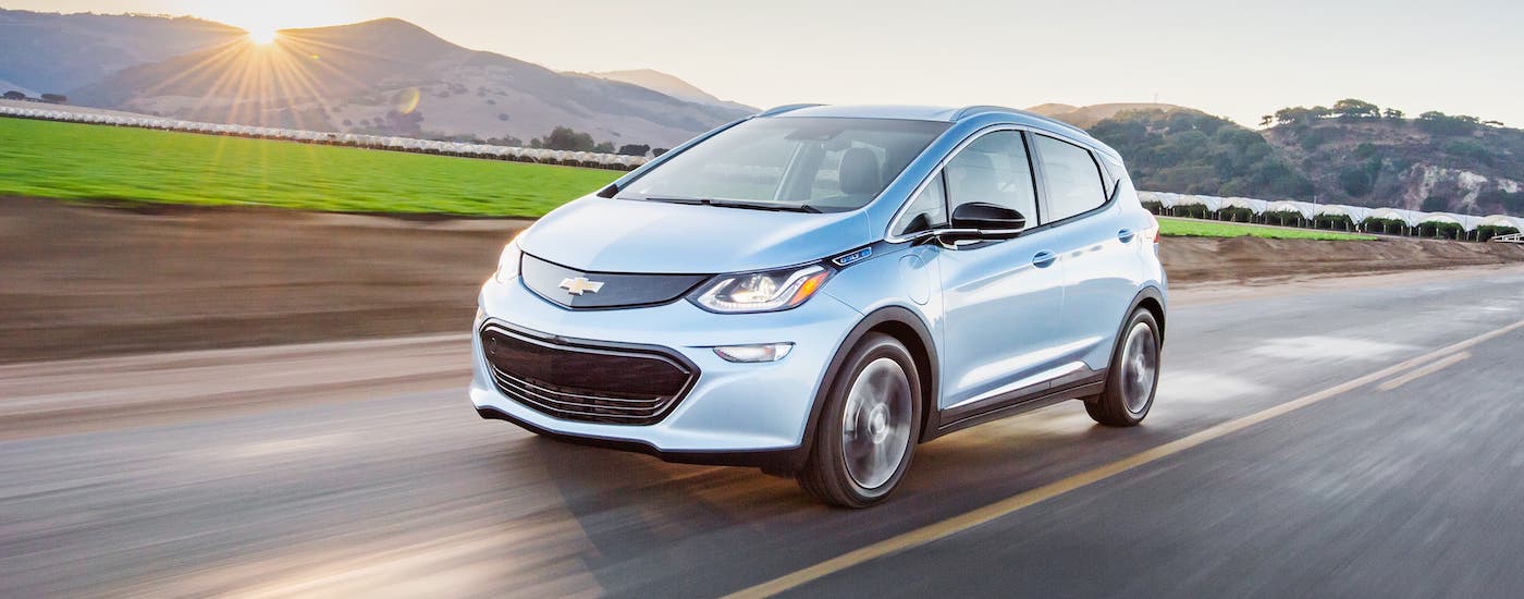 A silver 2018 Chevy Bolt EV is driving along a highway after leaving a used car dealership.