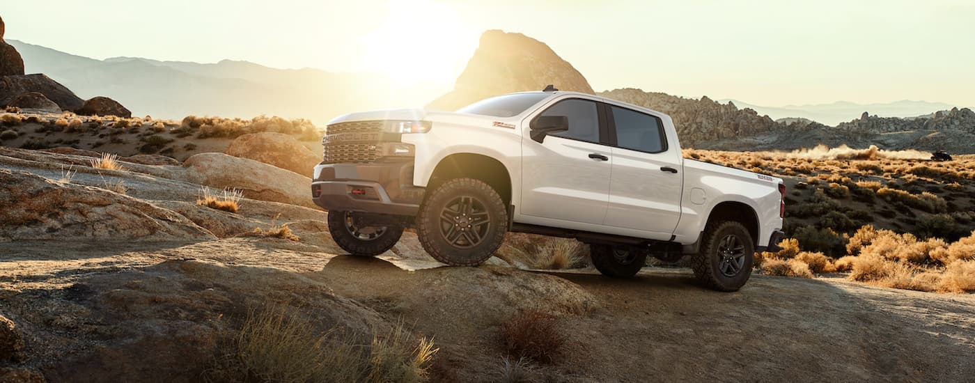 A white 2021 Chevy Silverado 1500 is off-roading on desert rocks after leaving a Chevy dealer.