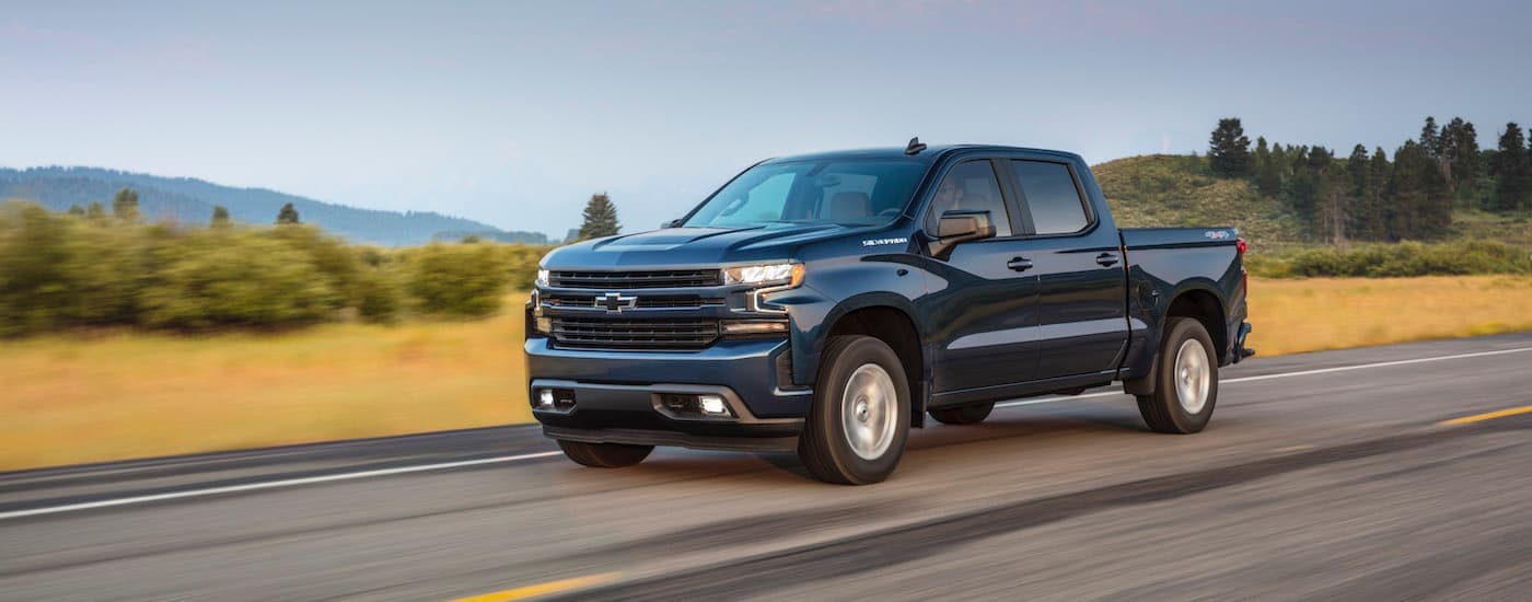 A blue 2020 Chevy Silverado 1500 is shown from the side driving on an open road after leaving a New Jersey used truck dealer.