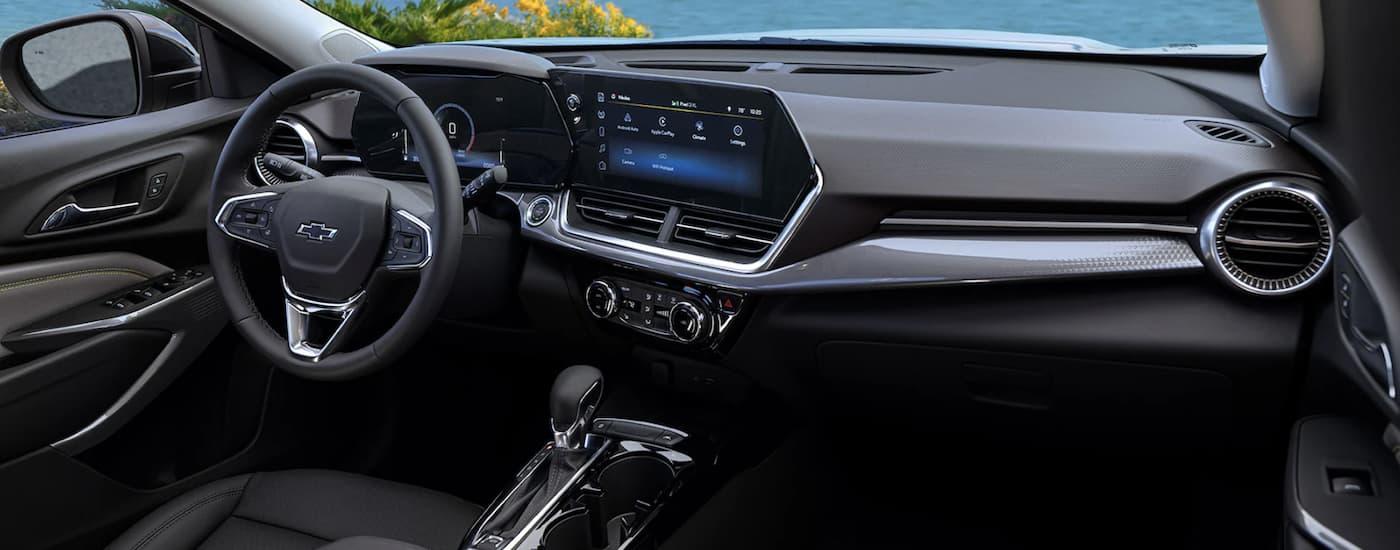 The black interior of a 2024 Chevy Trax shows the steering wheel and infotainment screen.