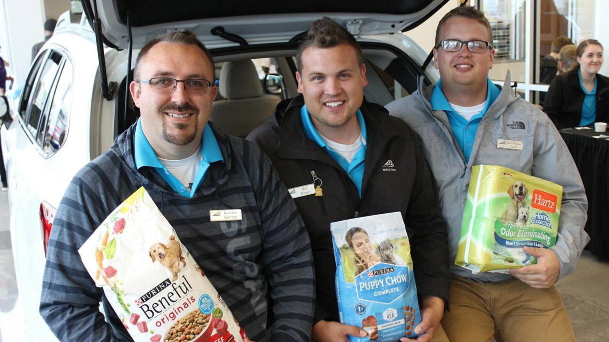 Three men smiling holding dog food