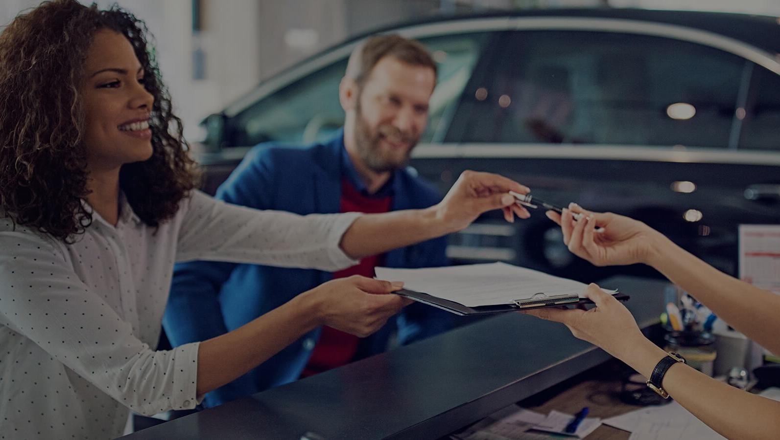 Smiling couple in a dealership, signing finance papers