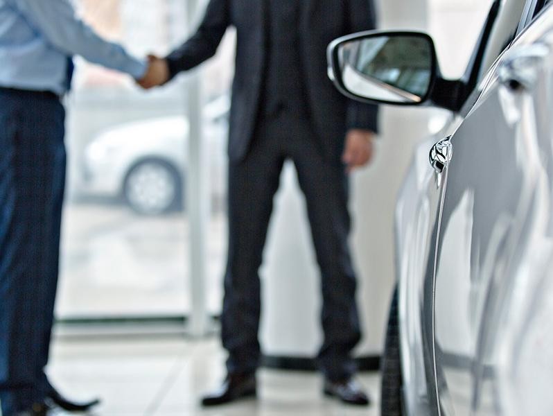 Men shaking hands in background. Vehicle in foreground.