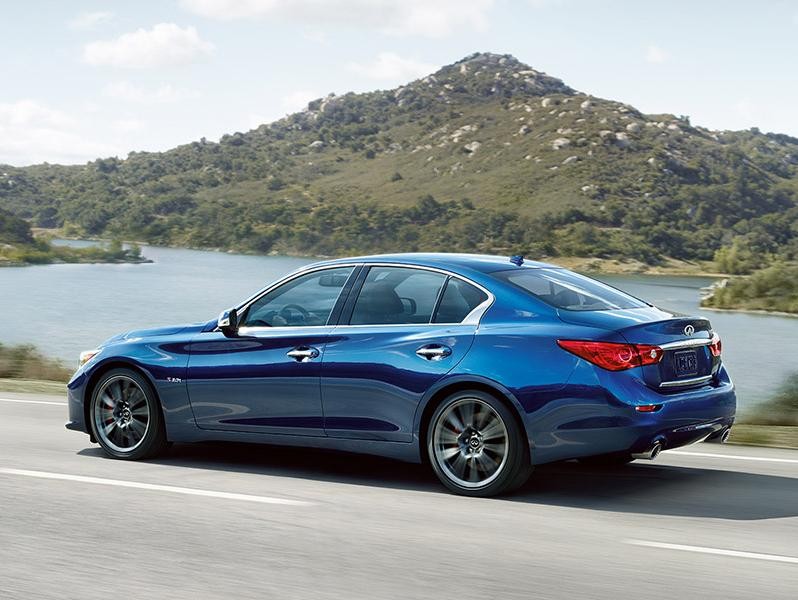 INFINITI 2017 Q50 driving on a highway next to a lake.