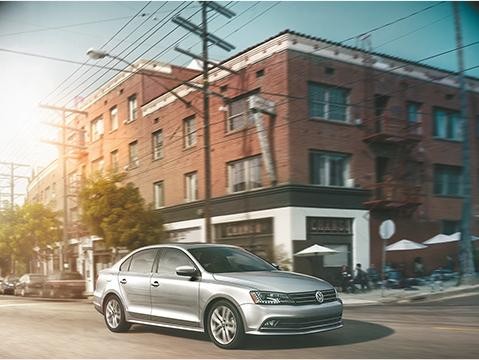 Silver VW Jetta driving down city street. 