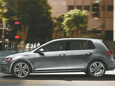 Side profile view of silver VW hatchback zooming down city street. 