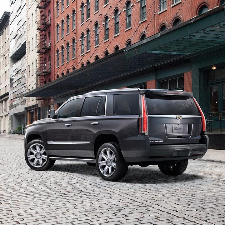 A grey Cadillac Escalade parked on a cobblestone city street.